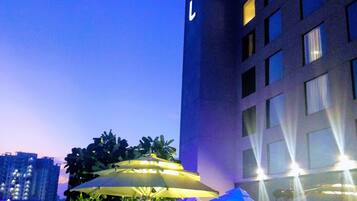 An outdoor seating area with umbrellas and tables, a building with a visible sign, and a view of the city skyline.