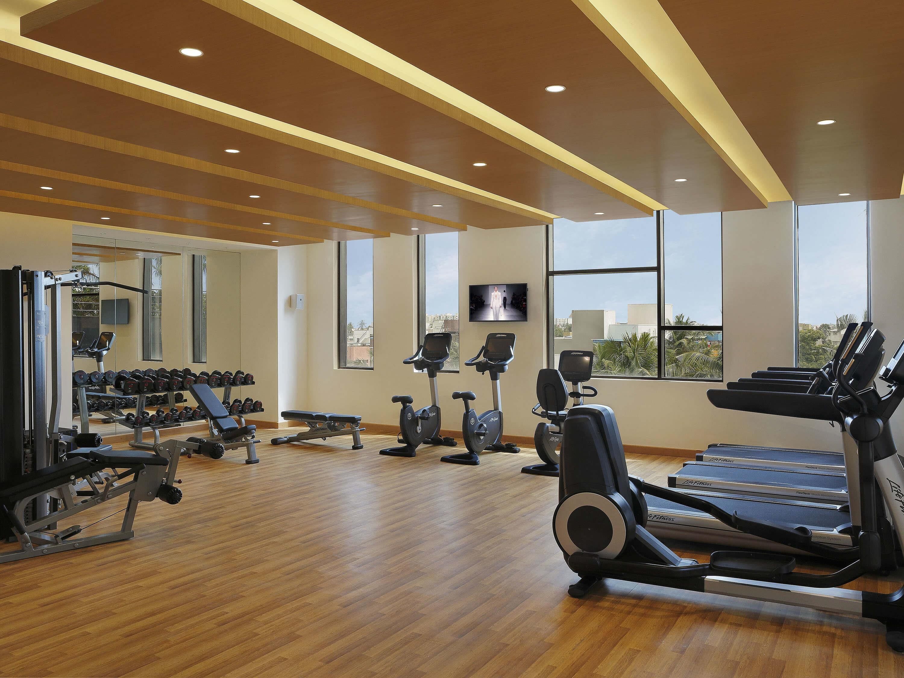 A gym with cardio machines, weightlifting equipment, and a TV screen.