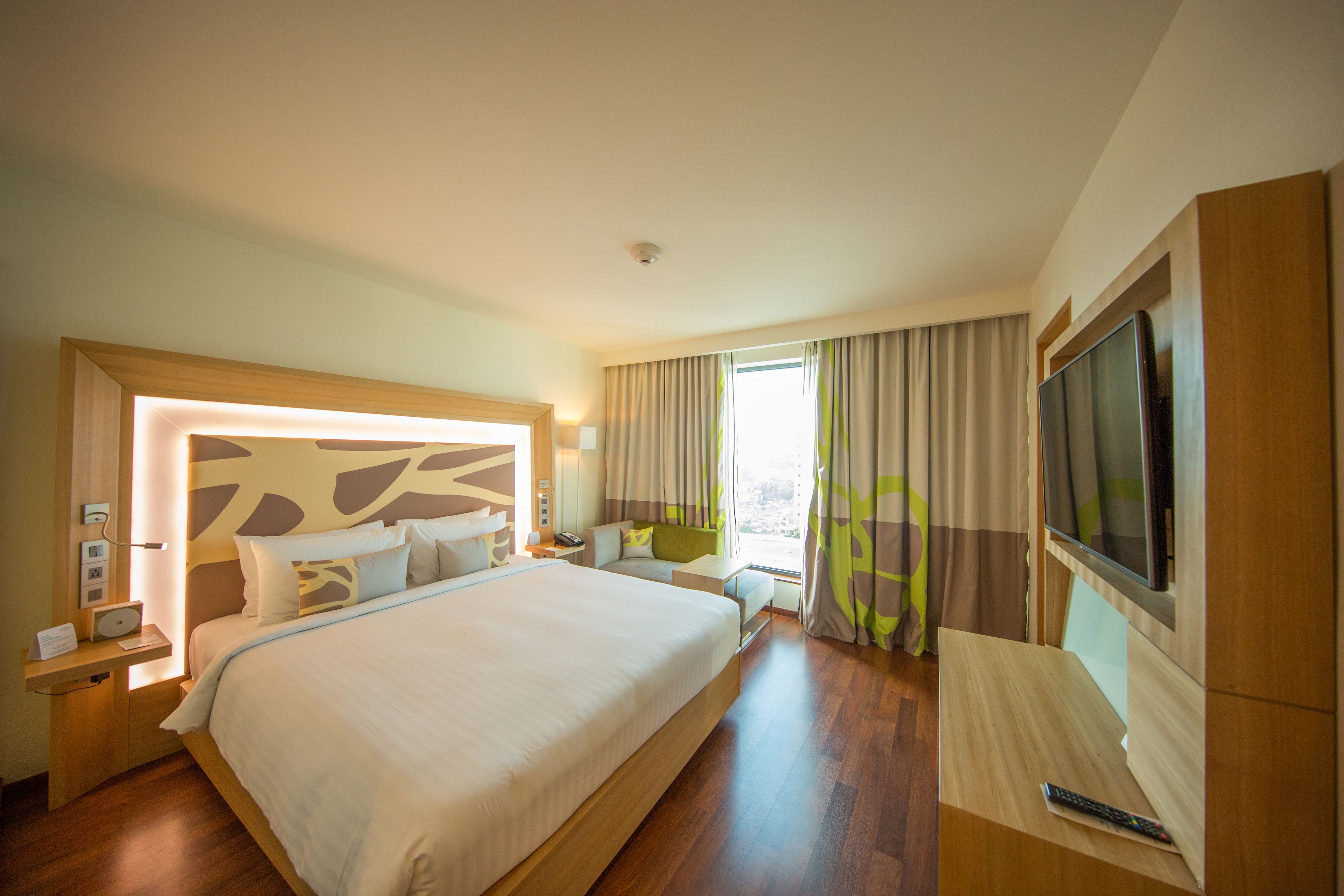 A hotel room with a large bed, bedside tables, a TV, and a window with curtains.