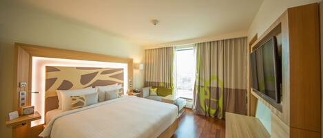 A hotel room with a large bed, bedside tables, a TV, and a window with curtains.
