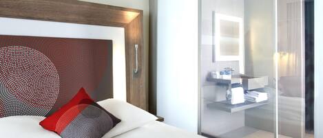 A hotel room with a bed, a large mirror, and a sliding glass door leading to a bathroom.