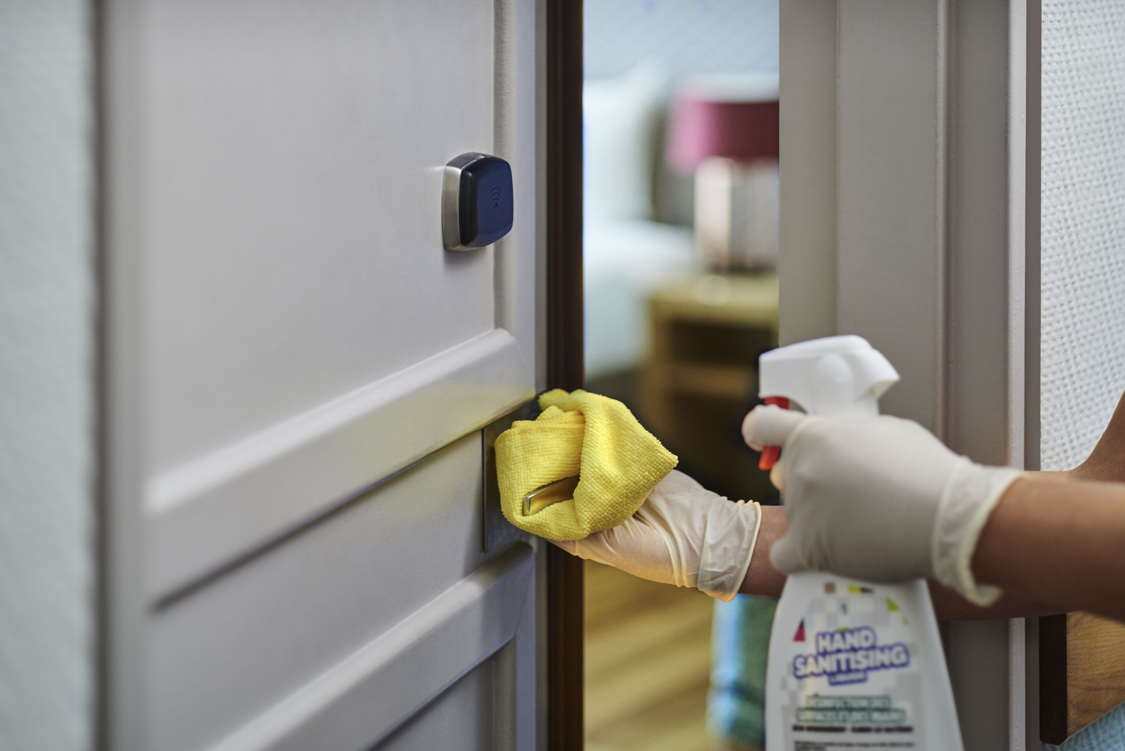 A person cleaning a door handle with a yellow cloth and a hand sanitizer bottle.