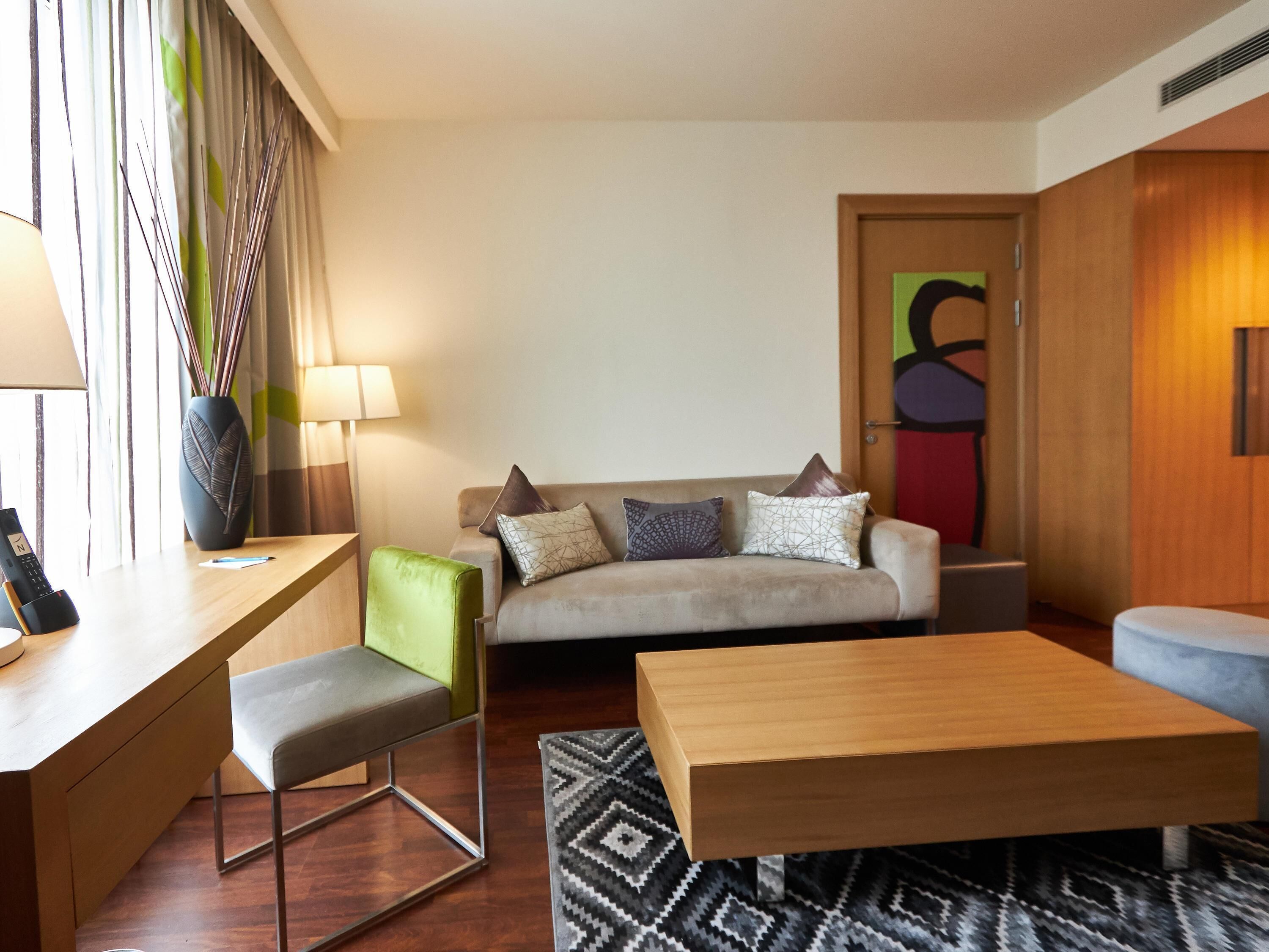 Una sala de estar moderna con un sofá, un sillón verde, una mesa de centro de madera y una lámpara.