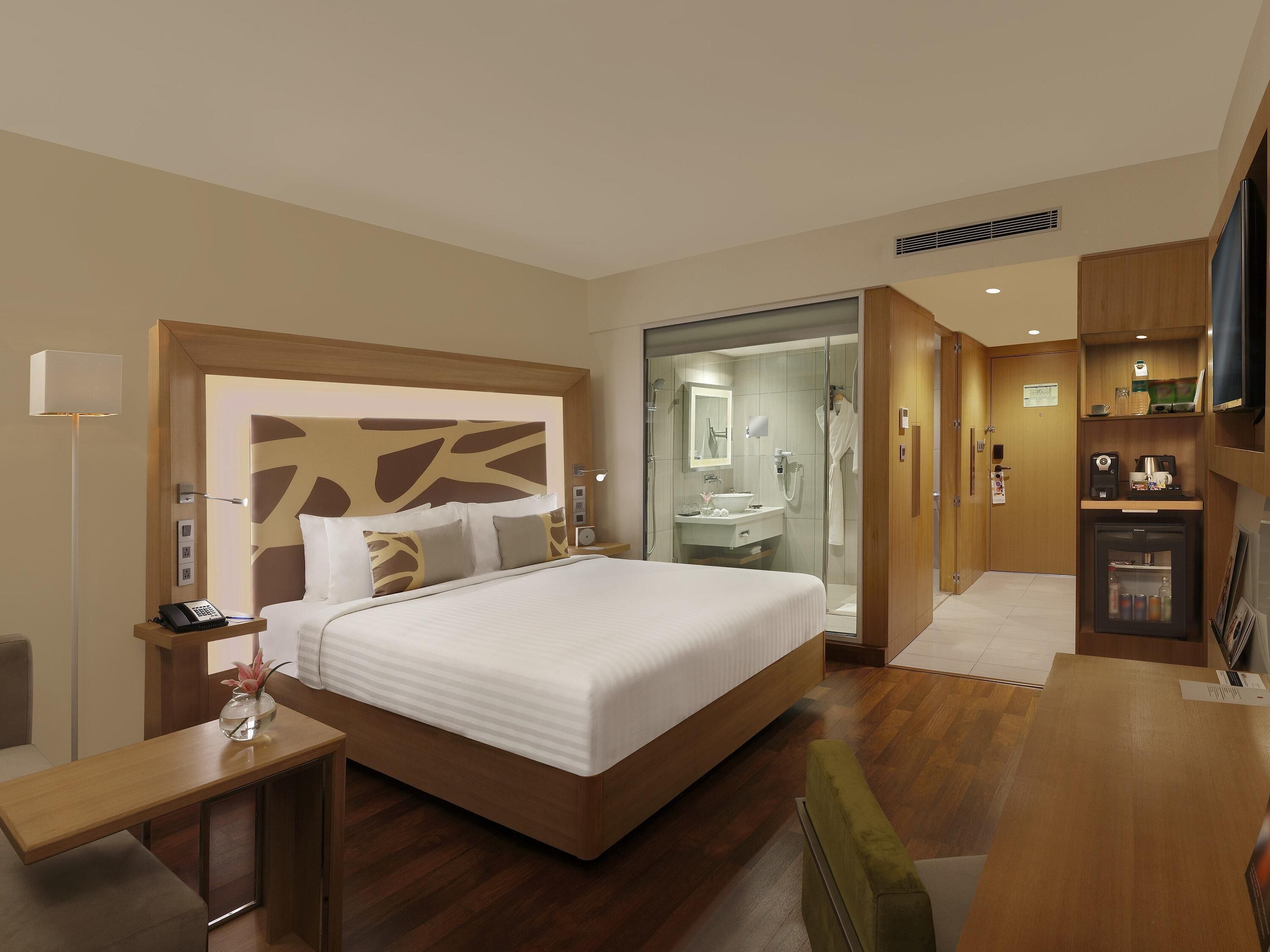 A hotel room with a large bed, a bedside table with a lamp, a shower area, a small kitchenette, and a TV.