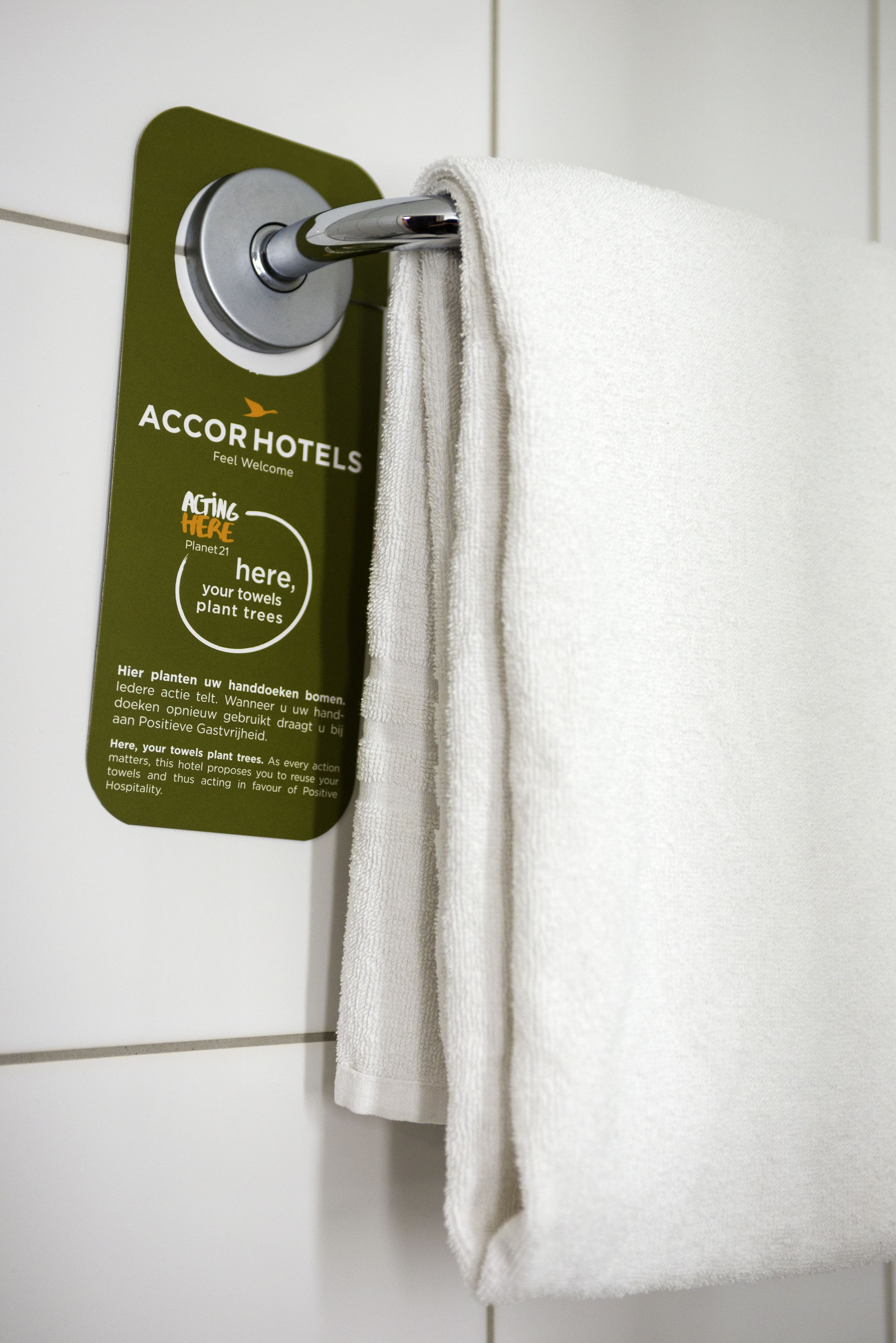 A towel hanging on a wall-mounted towel rack with a sign that reads "ACCORHOTELS" and a message about towel reuse.