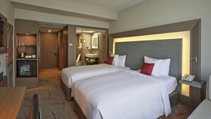 Habitación de hotel con dos camas, un minibar, un baño con espejo y una mesita de noche con teléfono.