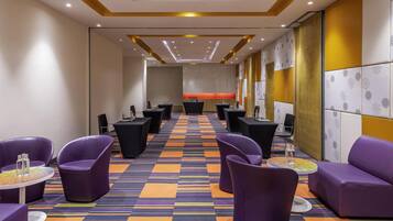 A hotel lobby with purple seating, a patterned carpet, and a long table with chairs.