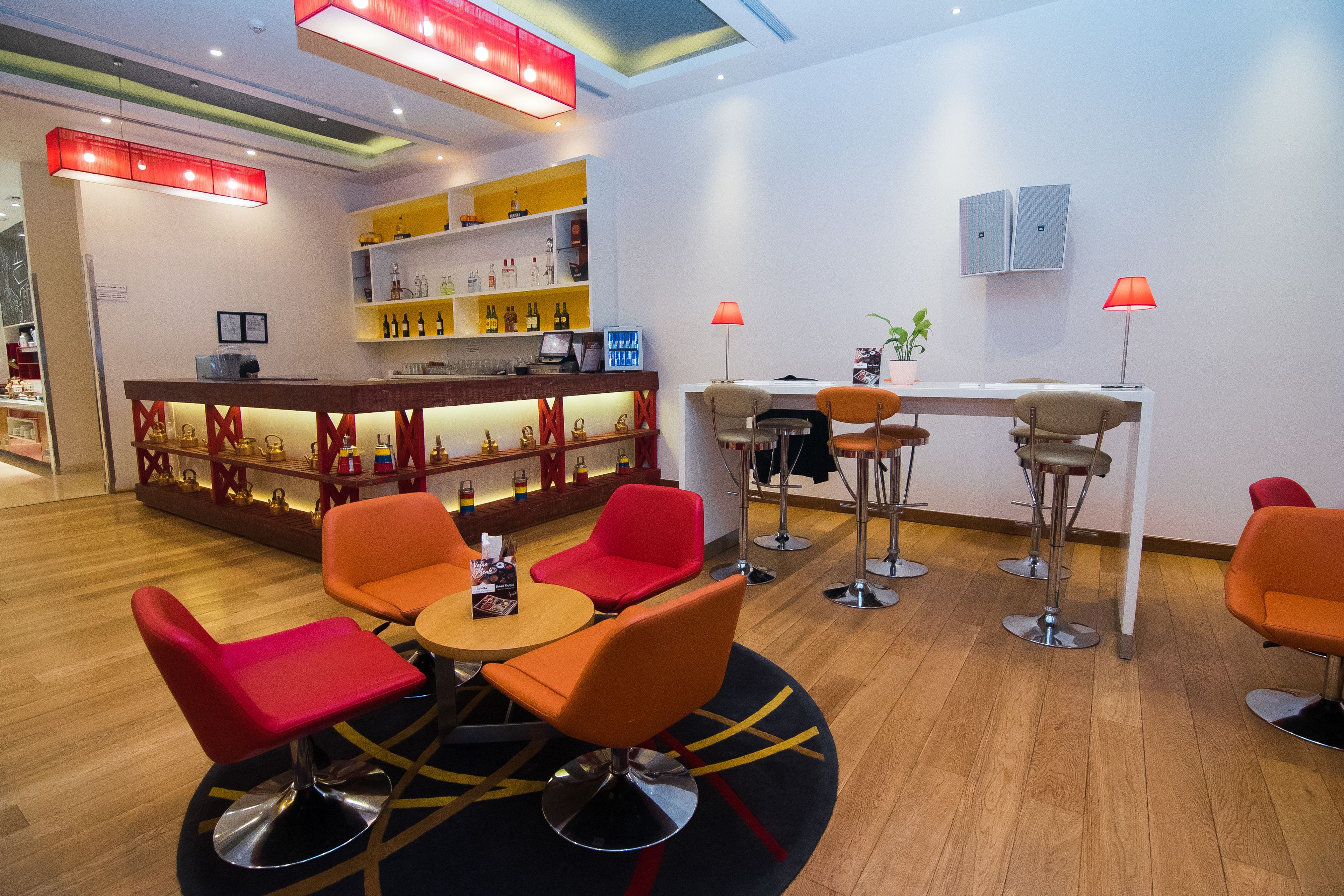Un espace bar moderne avec des chaises rouges et orange, un comptoir en bois et des étagères remplies de bouteilles.