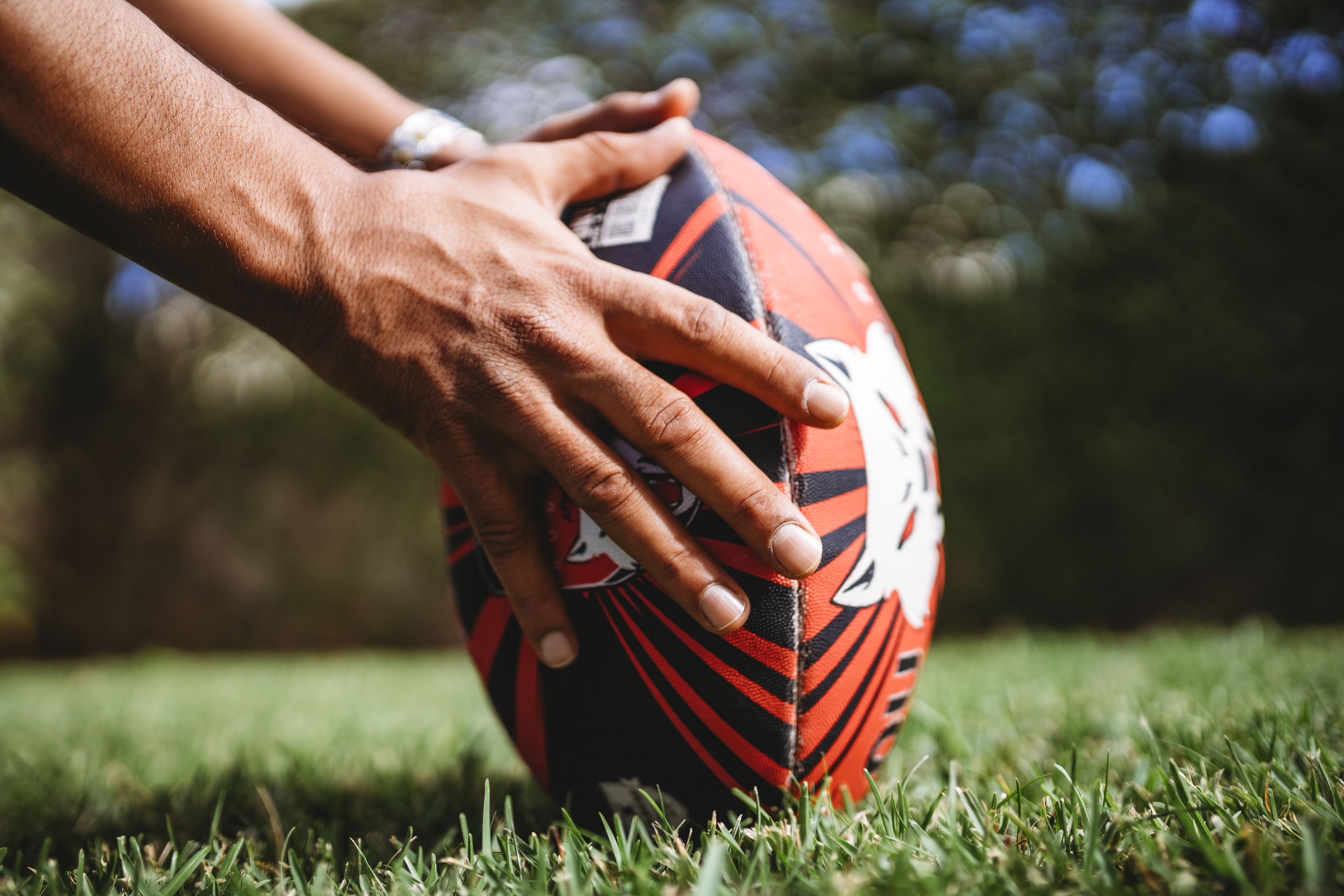 Een close-up van handen die een rugbybal vasthouden op het gras.