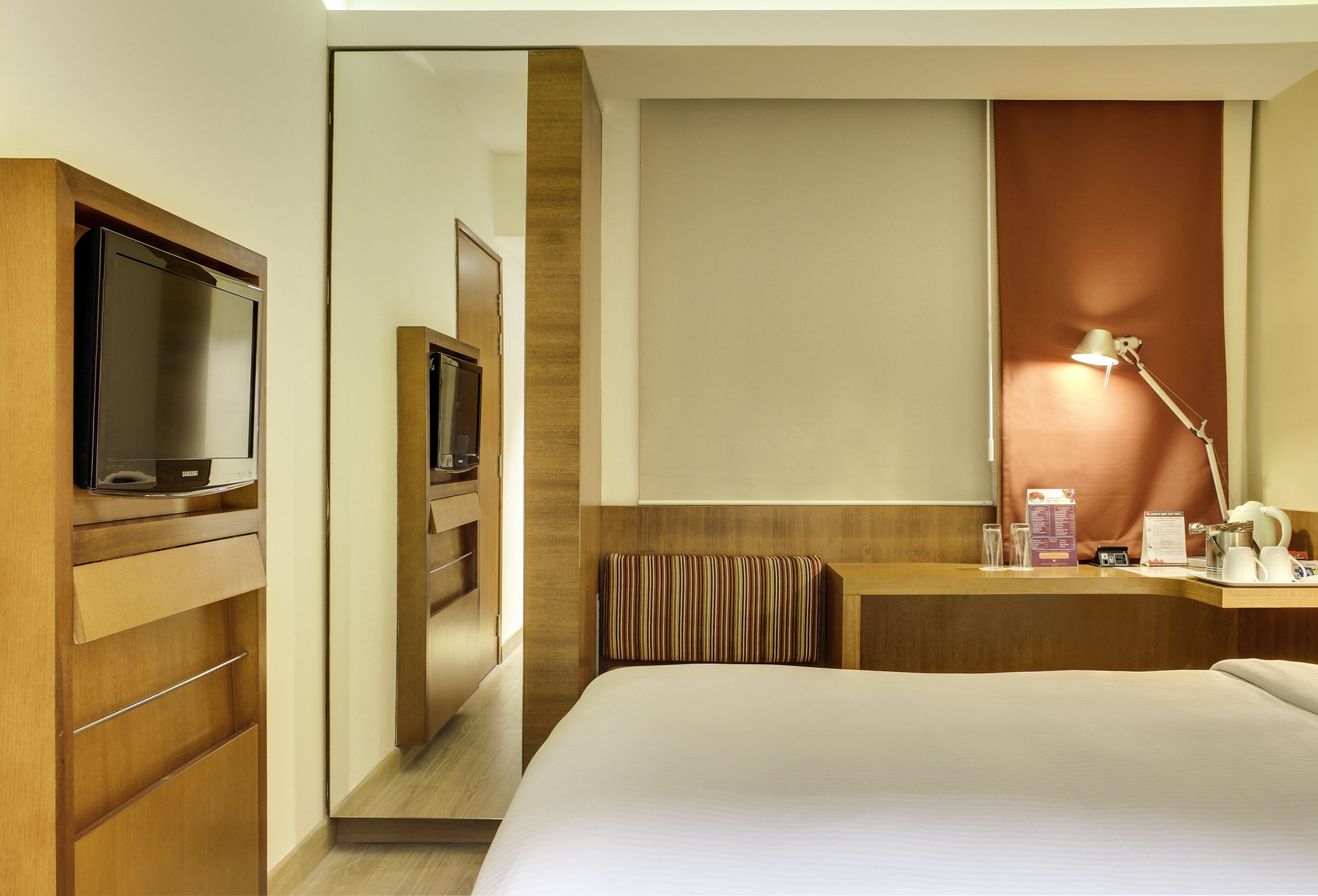 A hotel room with a bed, a television, a desk with a lamp, and a mirror.