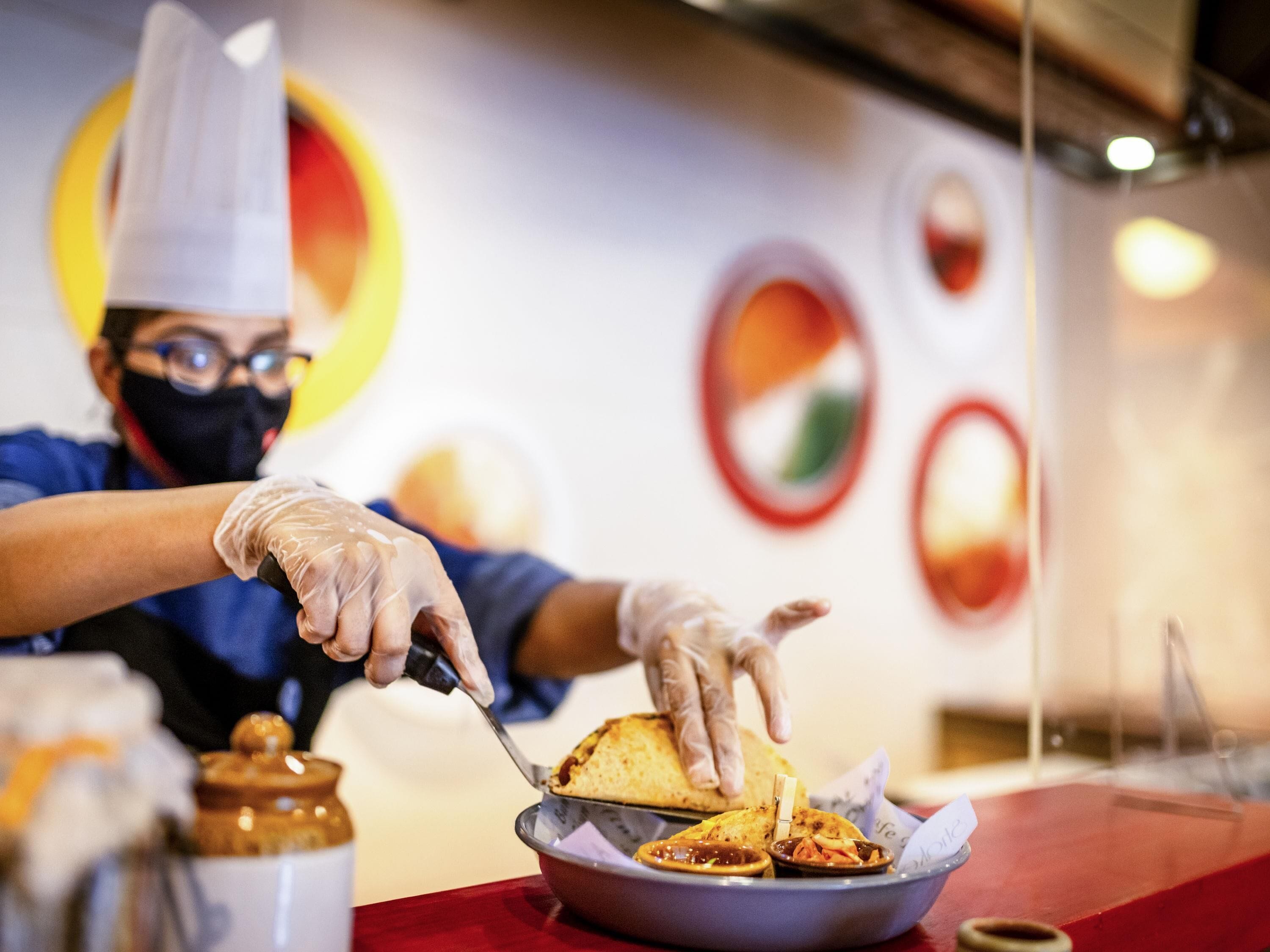 Una persona sirviendo comida, con guantes, sosteniendo un bol de comida y un plato sobre una mesa.