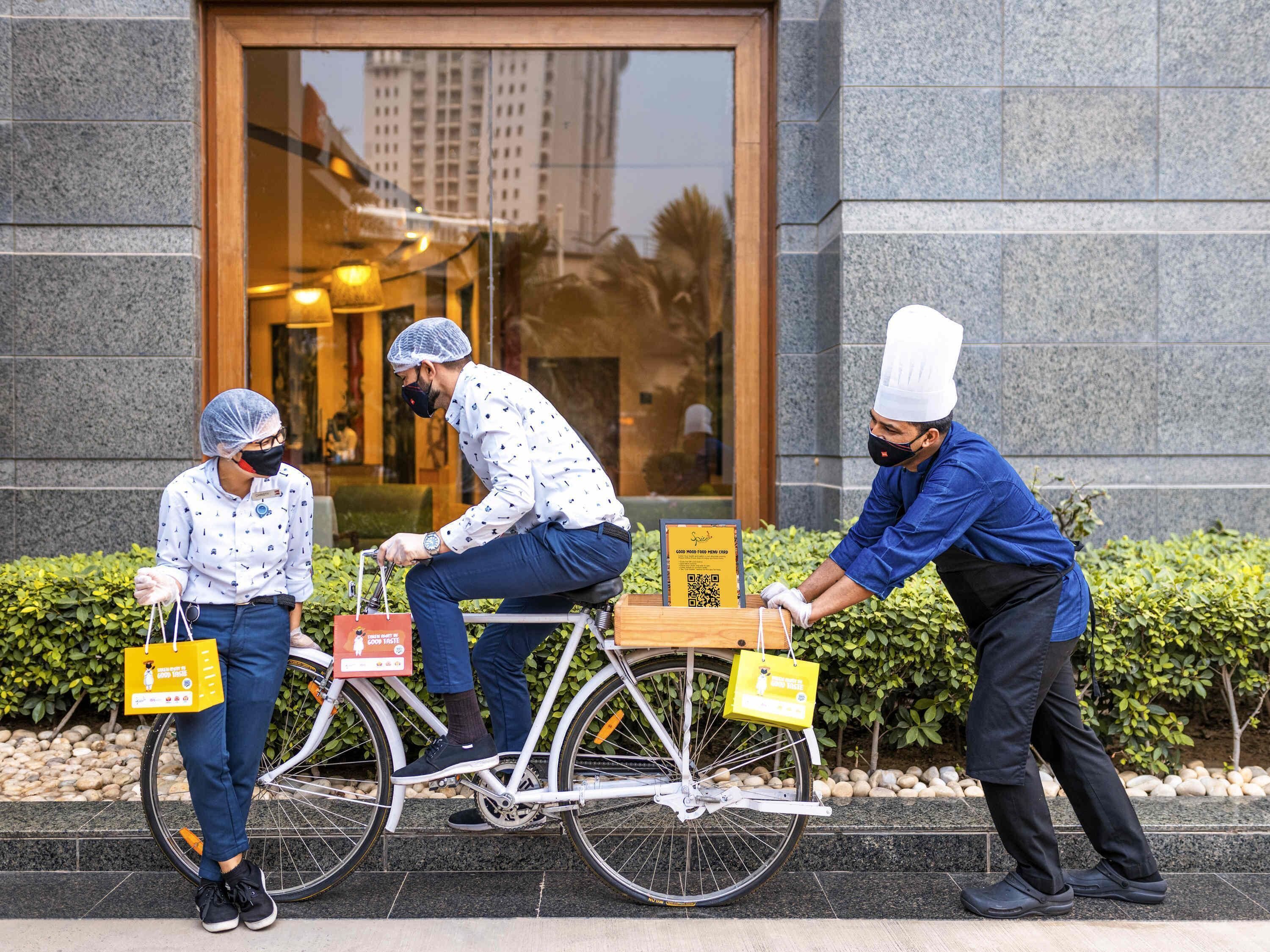 Three individuals with a delivery bike in front of a building with a large glass entrance.