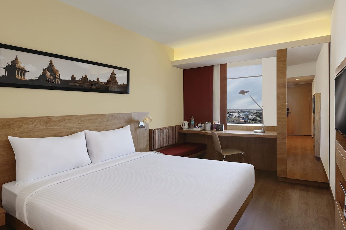 Ein Hotelzimmer mit einem großen Bett, einem Schreibtisch, einem Sessel, einem Fernseher und Blick auf die Stadt.