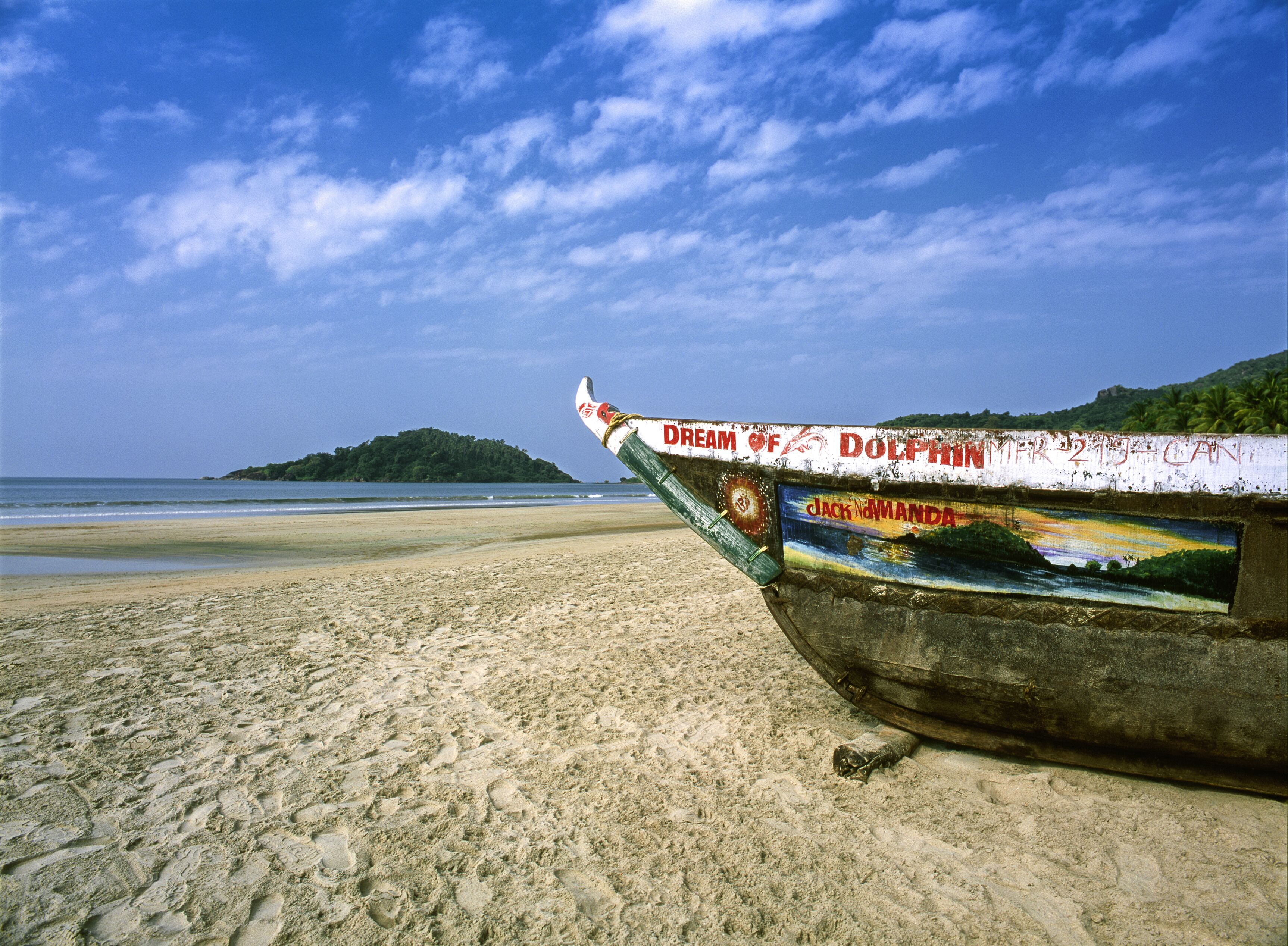 Um barco numa praia arenosa com um anúncio pintado e uma ilha ao longe.