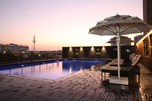 A swimming pool with lounge chairs and an umbrella, surrounded by a wooden deck and city views at sunset. - ibis Chennai OMR Hotel (Chennai)