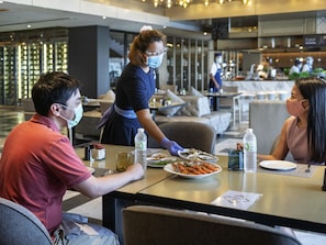 Zona pranzo con tavoli, sedie e un cameriere che serve.