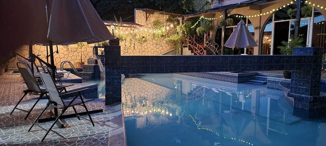 Une piscine extérieure dotée de chaises longues et de parasols, entourée d’un mur de pierre et de plantes.