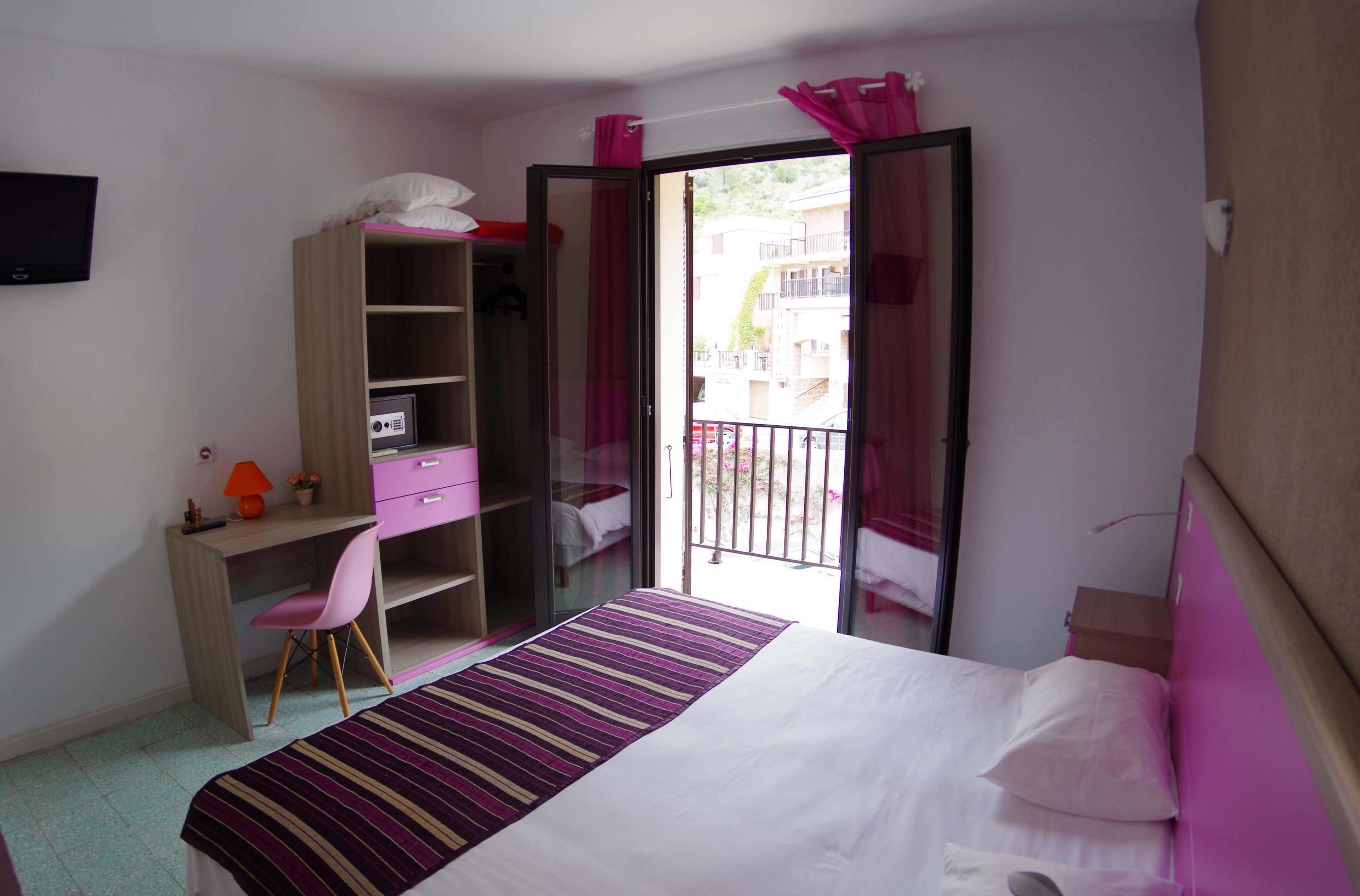 A bedroom with a bed, a desk, a chair, a wardrobe, and a balcony with a view.
