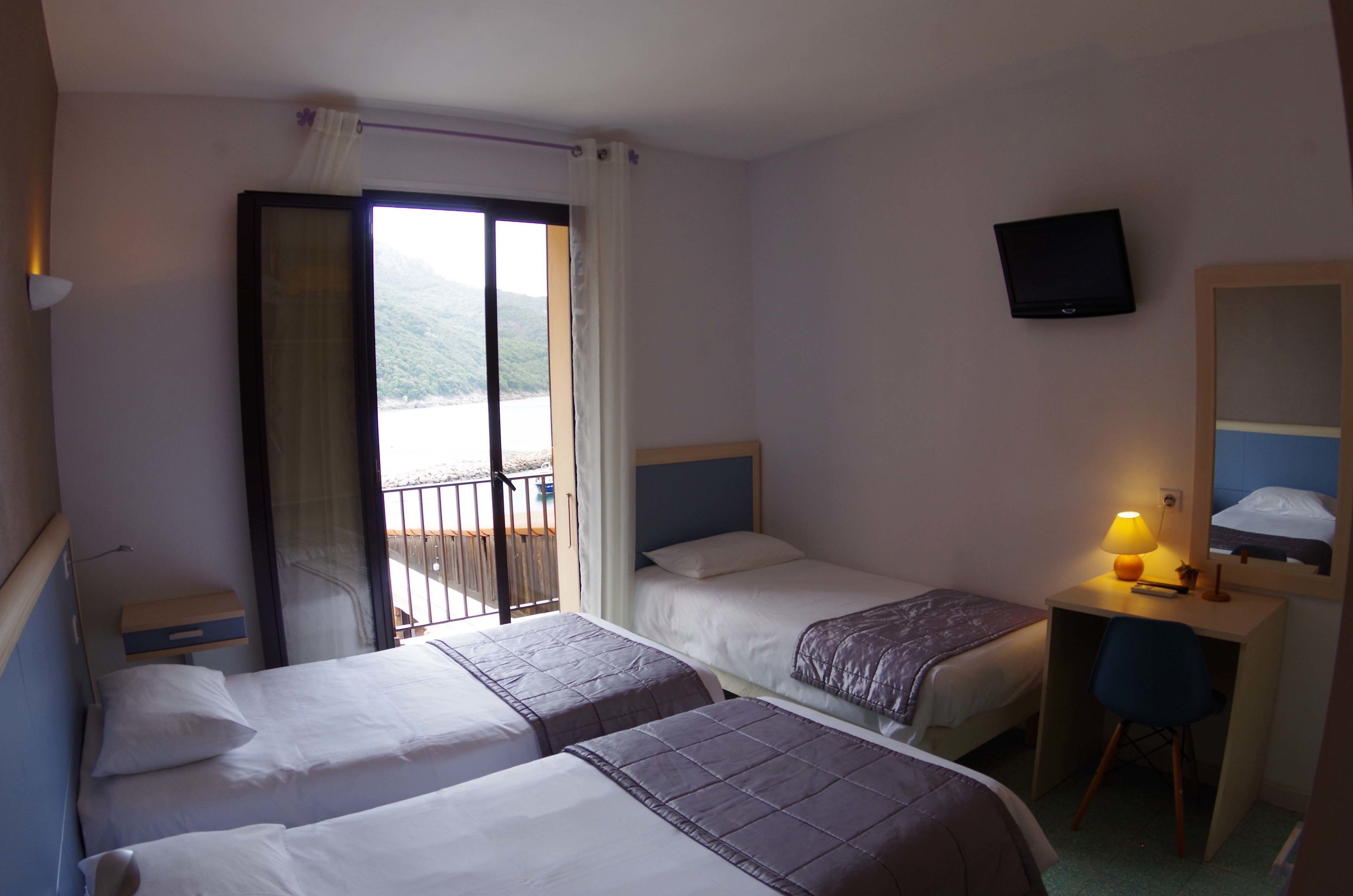 Une chambre d’hôtel avec deux lits, un bureau avec une chaise, une télévision et un balcon avec vue.