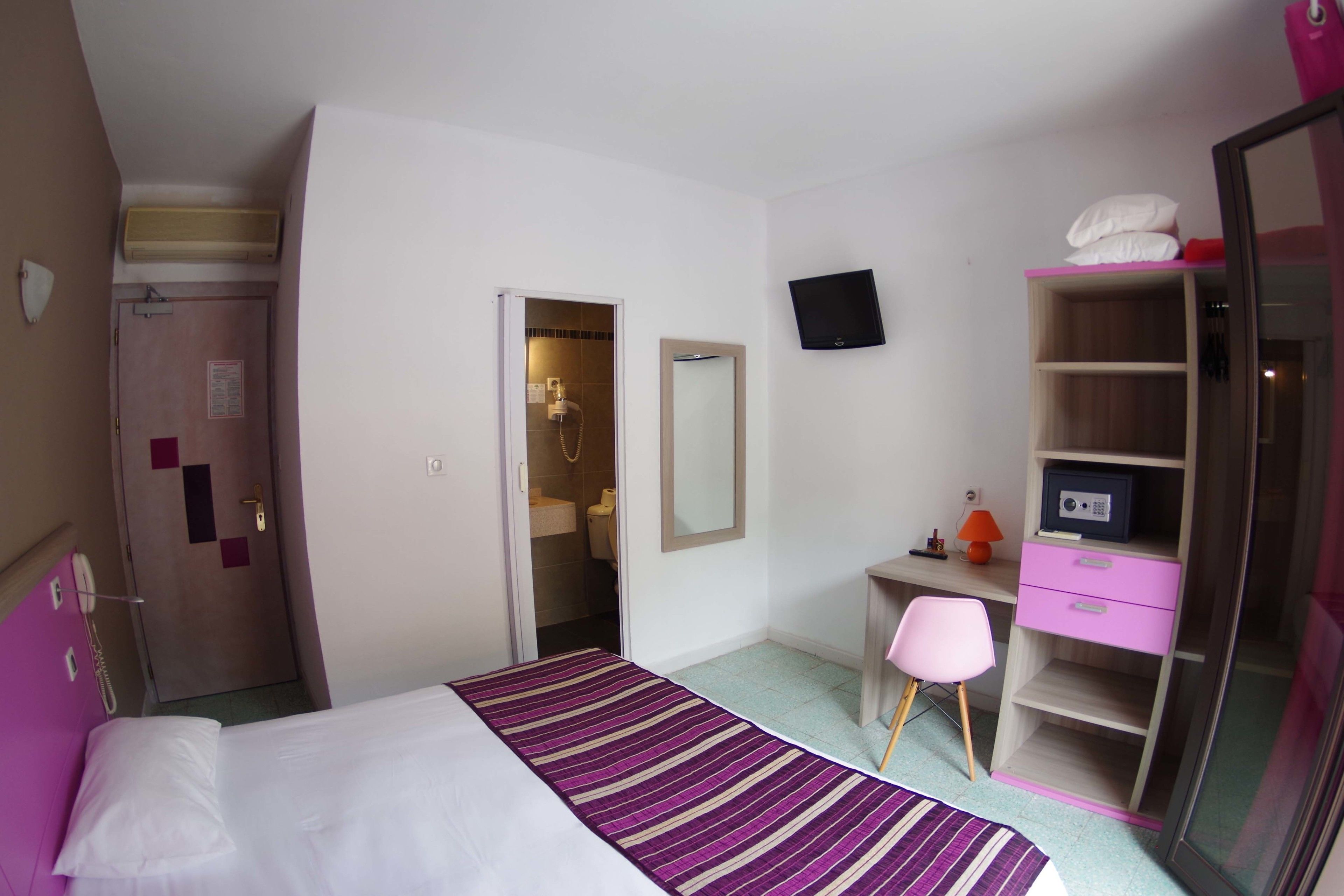 A hotel room with a bed, a desk with a chair, a wardrobe, a mirror, and a television.