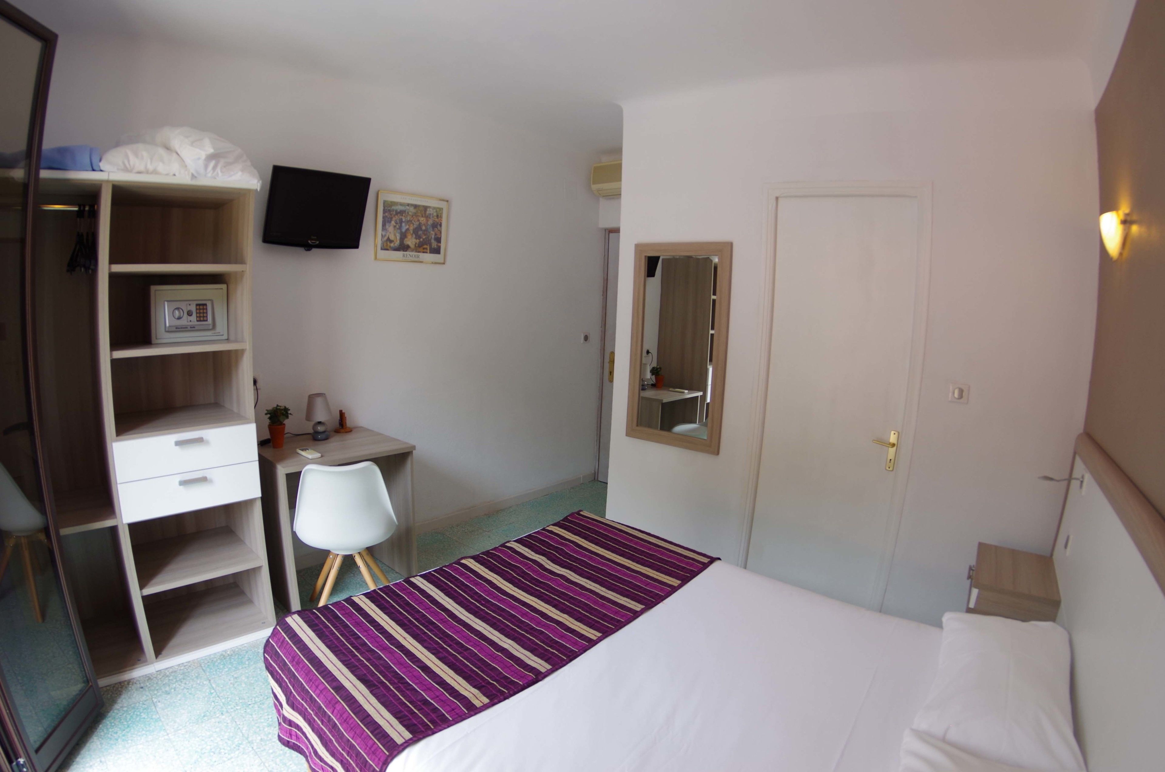 Ein Hotelzimmer mit Bett, Schreibtisch, Stuhl, Kleiderschrank, Fernseher und Spiegel.