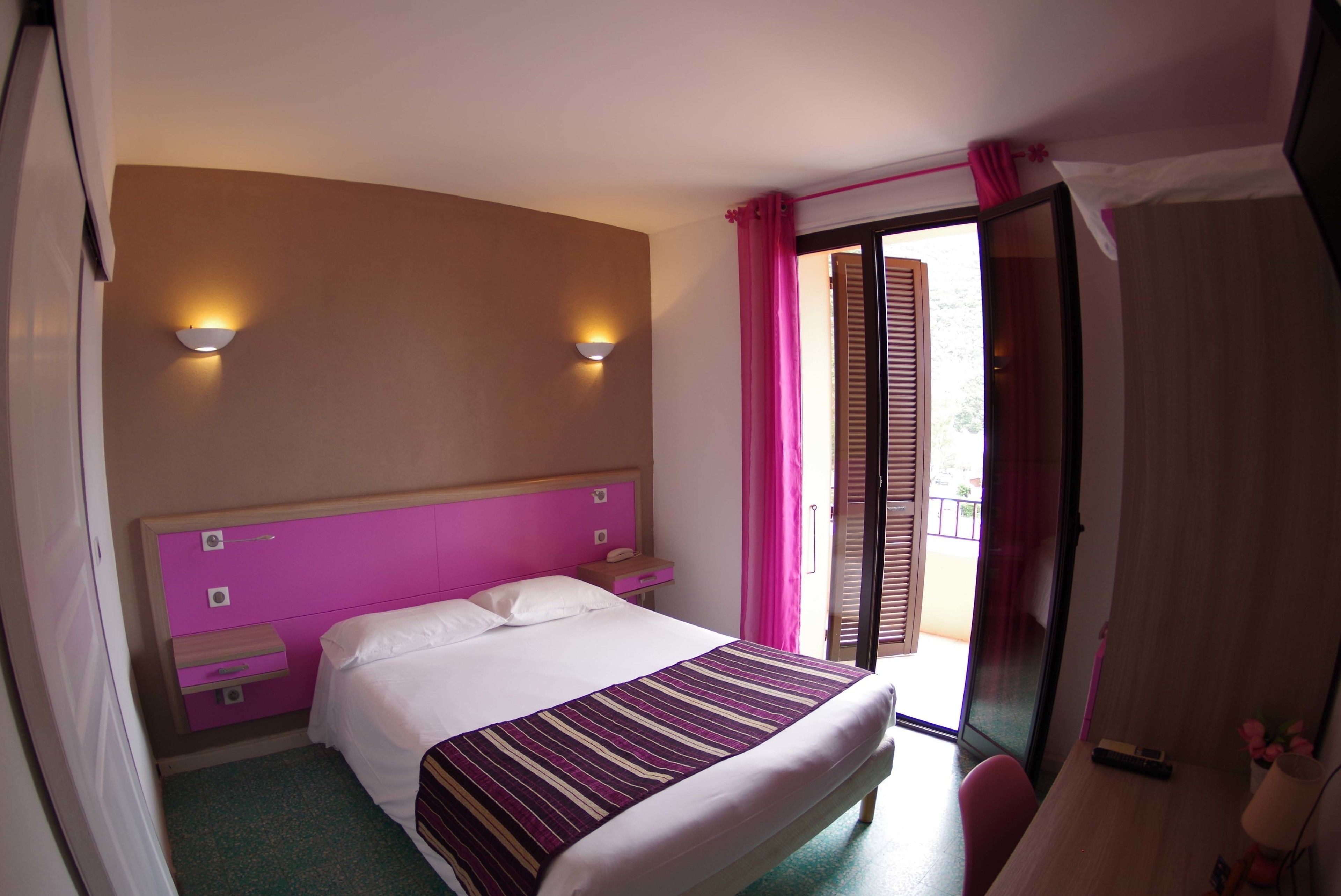 A hotel room with a bed, a nightstand, a desk, and a window with curtains.