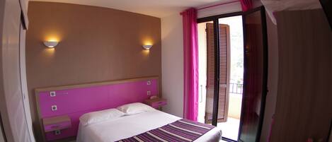 Una habitación de hotel con cama, mesita de noche, escritorio y ventana con cortinas.