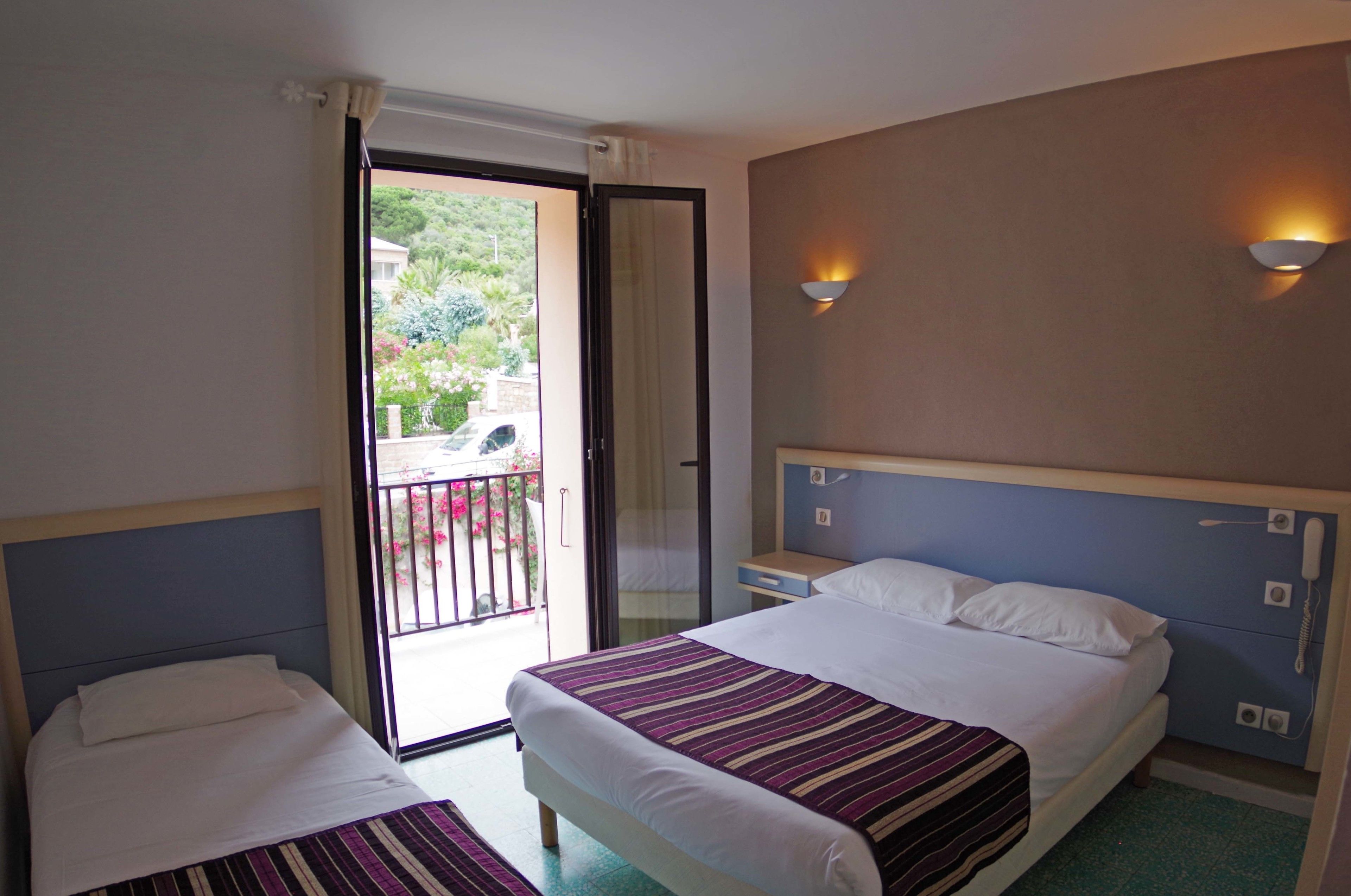 A hotel room with two beds, a balcony, and a wall-mounted phone.