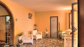 A lobby with a tiled floor, white wicker furniture, potted plants, and a door with a frosted glass panel.