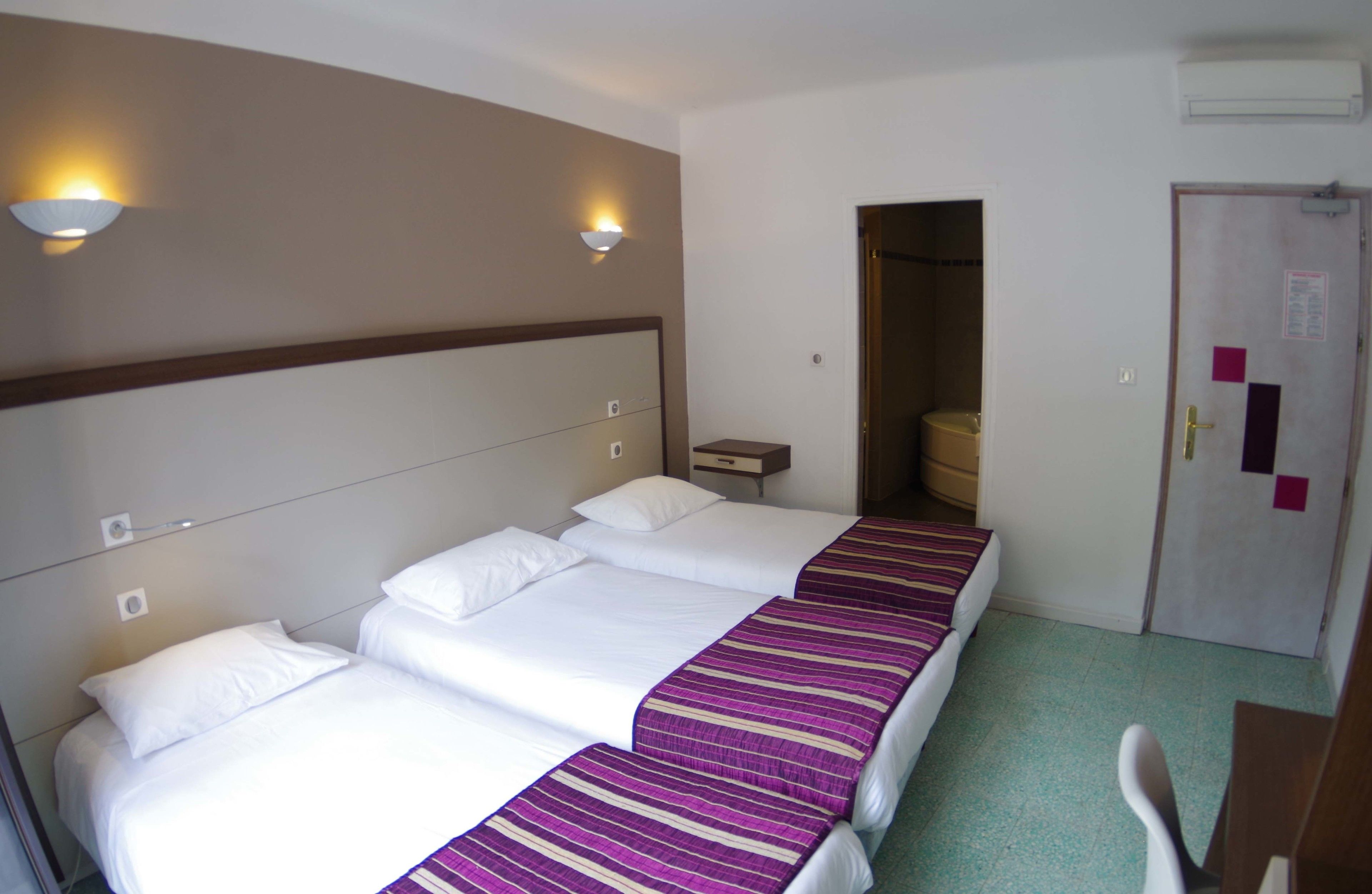 Habitación de hotel con cuatro camas, una mesita de noche pequeña, un escritorio y una silla.