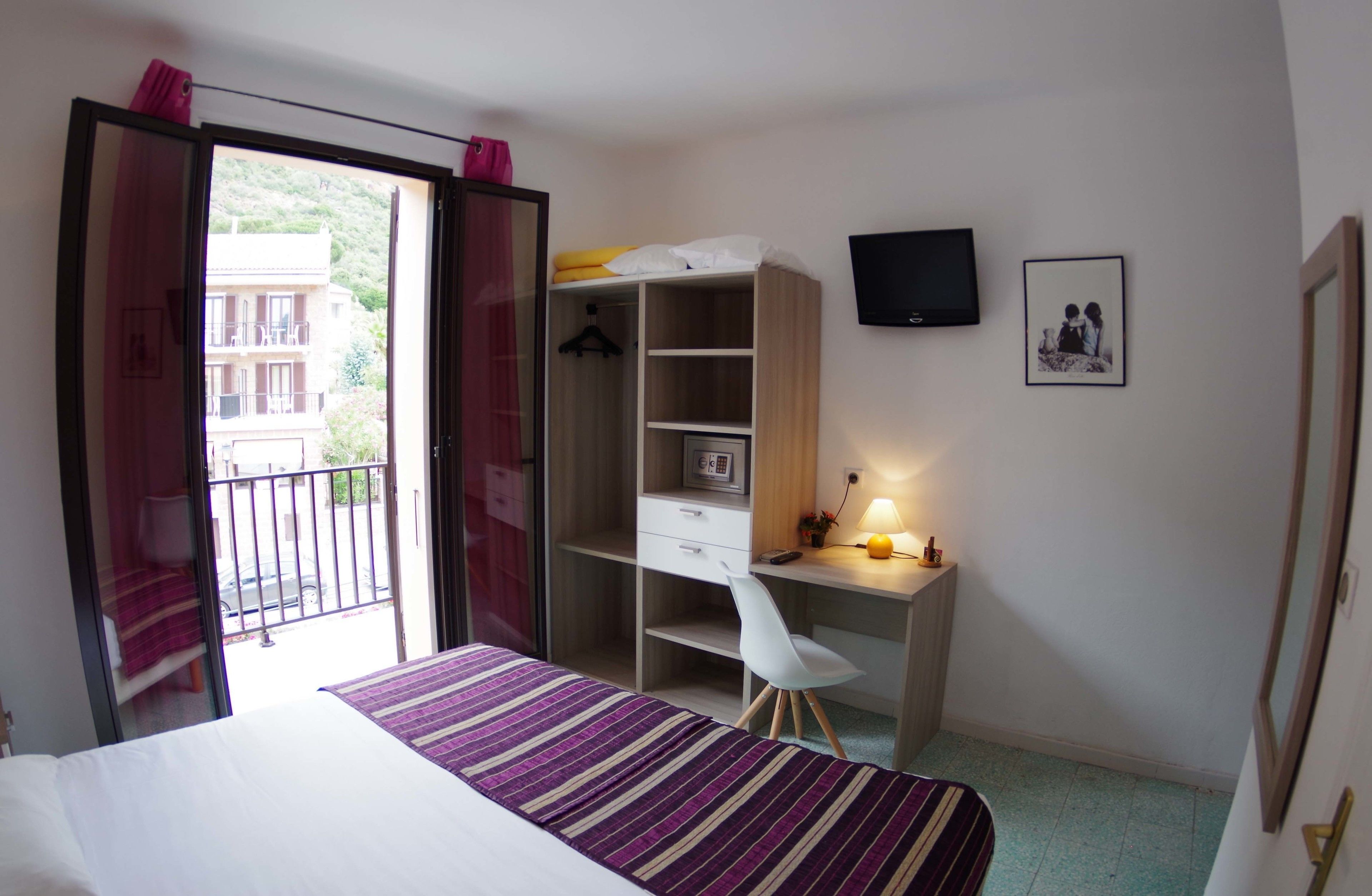 A bedroom with a bed, a desk, a chair, a wardrobe, a TV, and a balcony.