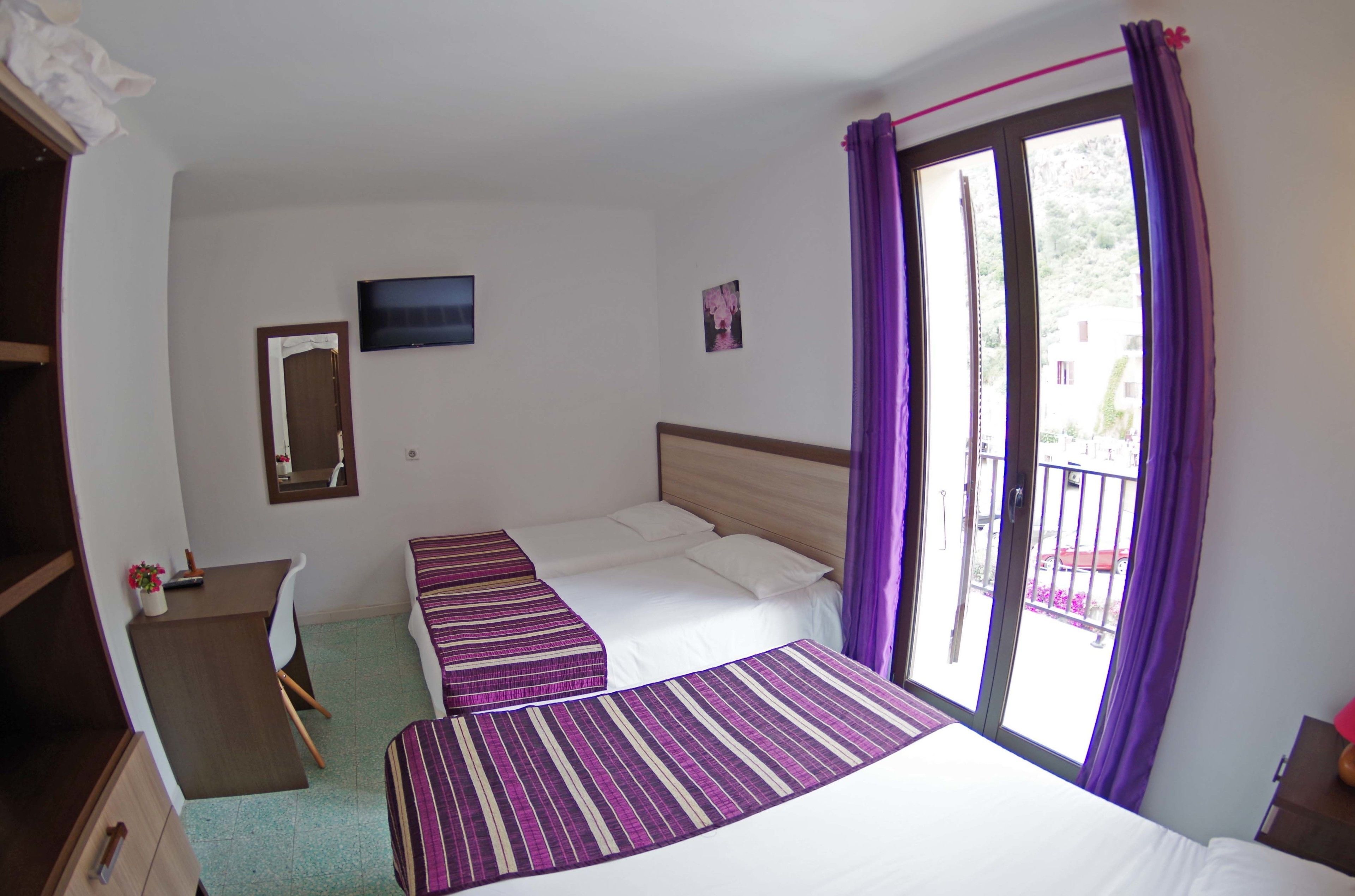 A room with two beds, a desk, a chair, a TV, and a balcony with purple curtains.