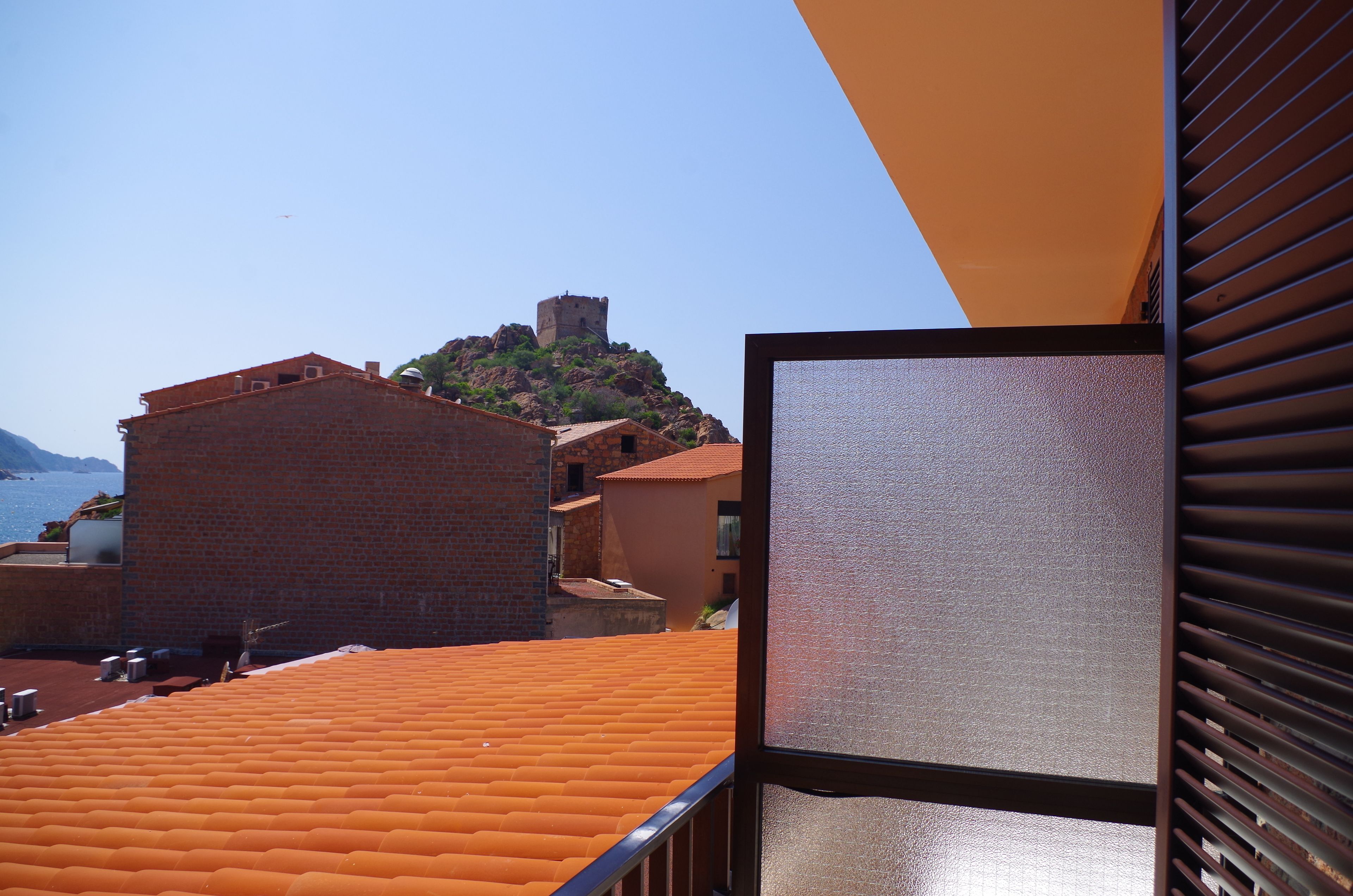 A view from a balcony with a tiled roof, overlooking a historic stone building with a tower, and a clear sky.