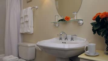 A bathroom with a white sink, a toilet, a glass shelf with a rose, and a white cup on a small table.