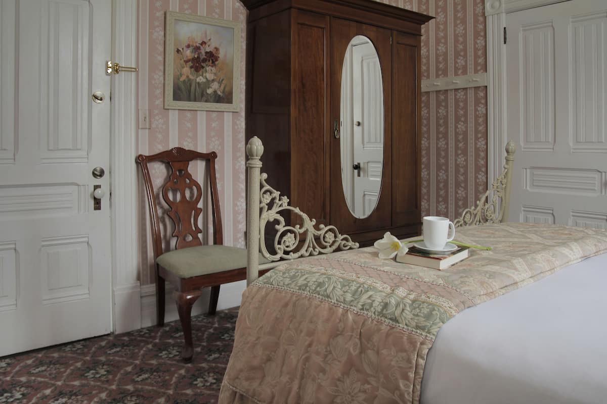 A bedroom with a bed, a wooden chair, a wardrobe, and a painting on the wall.
