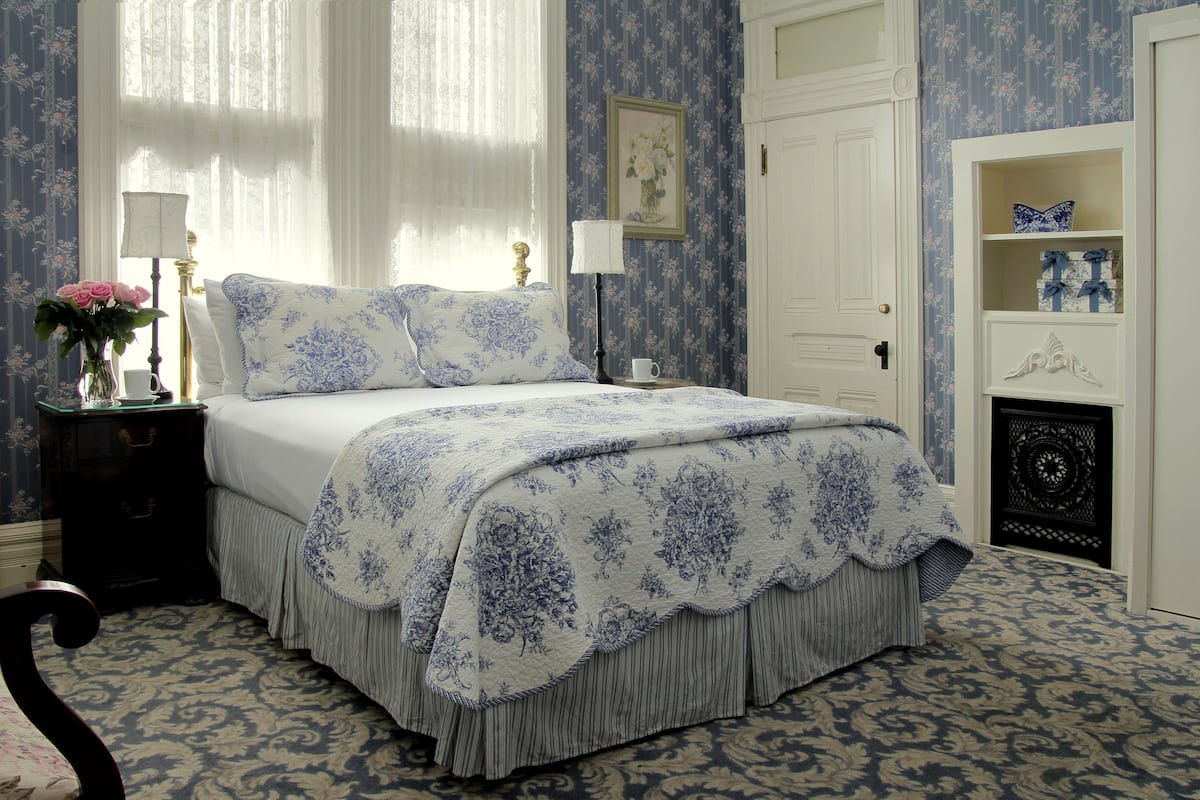 A bedroom with a bed, nightstand, lamp, vase with flowers, and a door with a decorative panel.