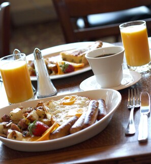 A breakfast setting with plates of food, a cup of coffee, and glasses of orange juice on a wooden table.