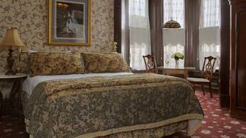 Une chambre à coucher avec un grand lit, un bureau avec une chaise, une lampe et un tableau au mur.