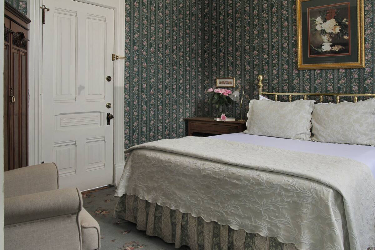 A bedroom with a large bed, a nightstand, a framed picture, and a door.