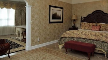 Un dormitorio con una cama grande, un banco, un cuadro enmarcado en la pared y una ventana con cortinas.