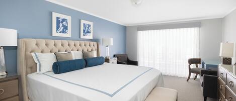 A hotel room with a large bed, a desk, a chair, and a bench.