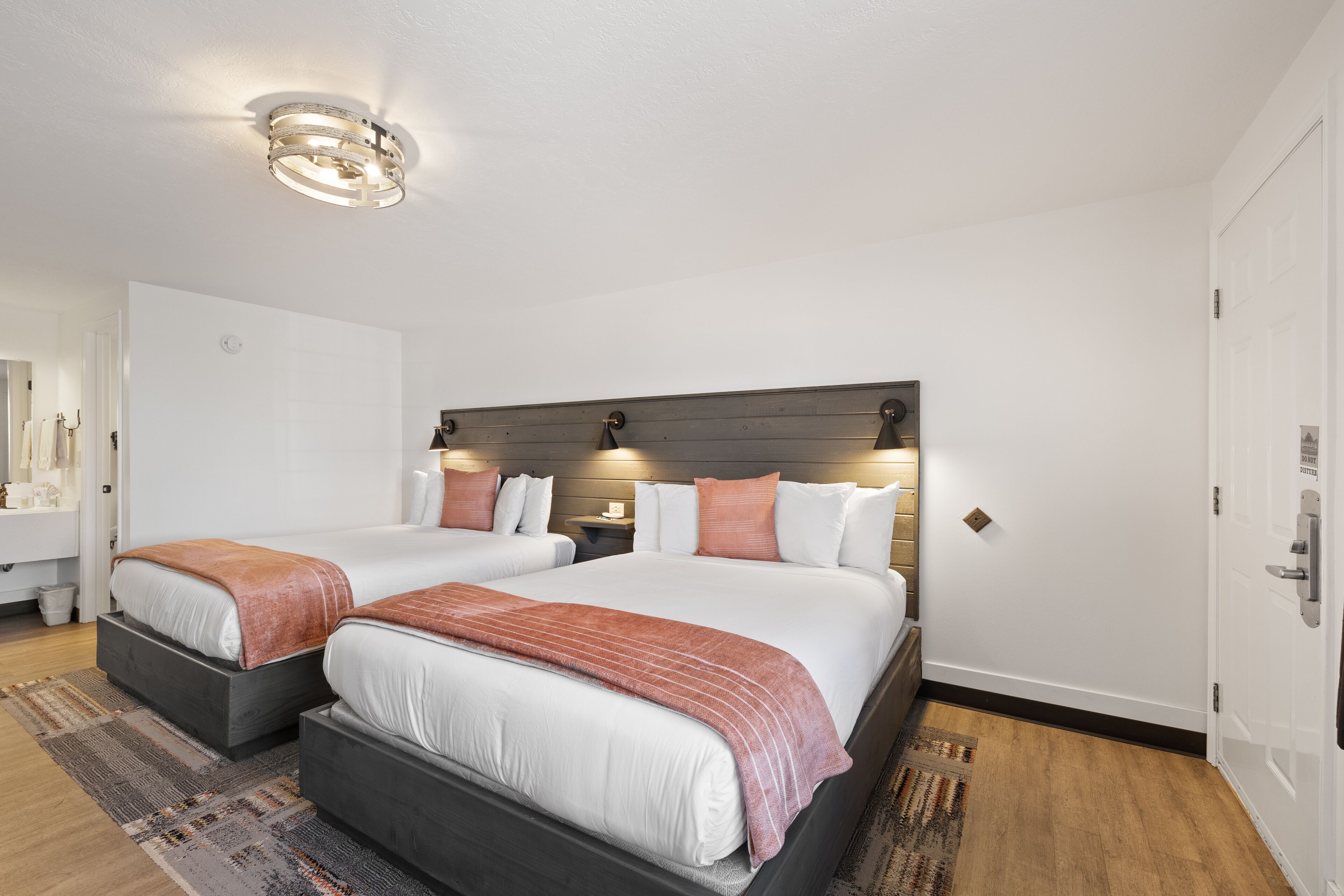 Habitación de hotel con dos camas, cabecero de madera, una mesita de noche y un baño a simple vista.