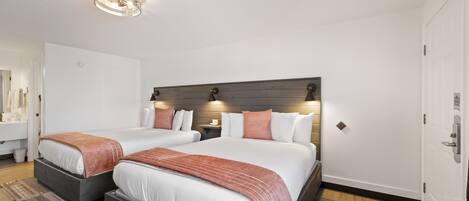 Habitación de hotel con dos camas, cabecero de madera, una mesita de noche y un baño a simple vista.