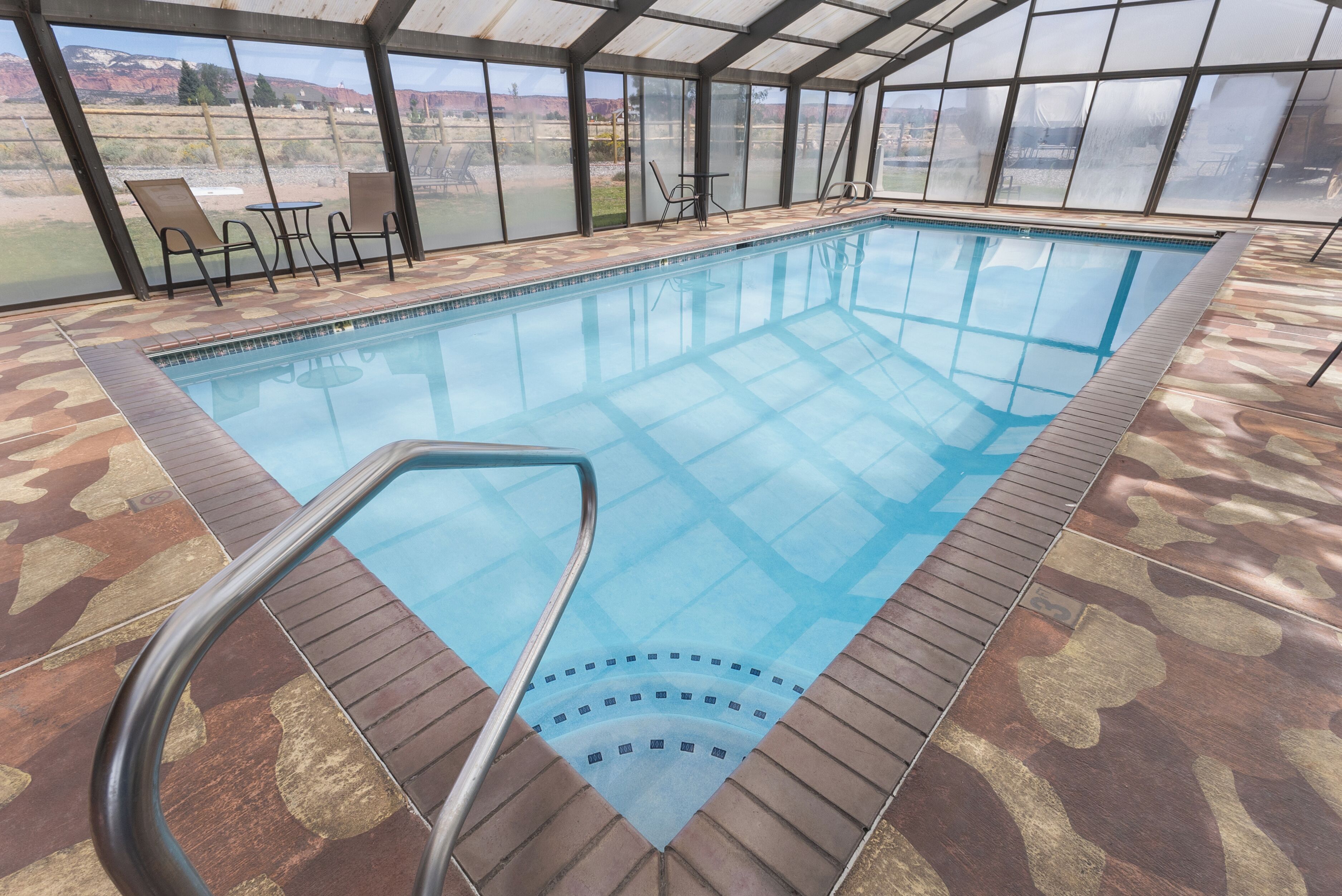 An indoor swimming pool with clear glass walls, a wooden deck, and a view of the outdoors.