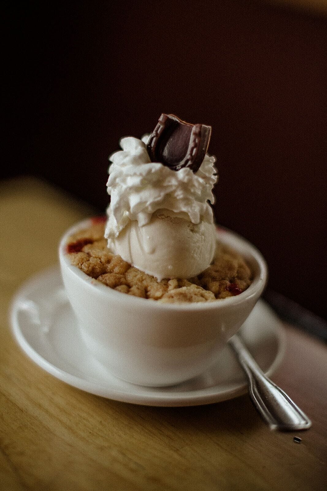 Un dessert servi dans un bol blanc, posé sur une soucoupe, avec une cuillère à côté.