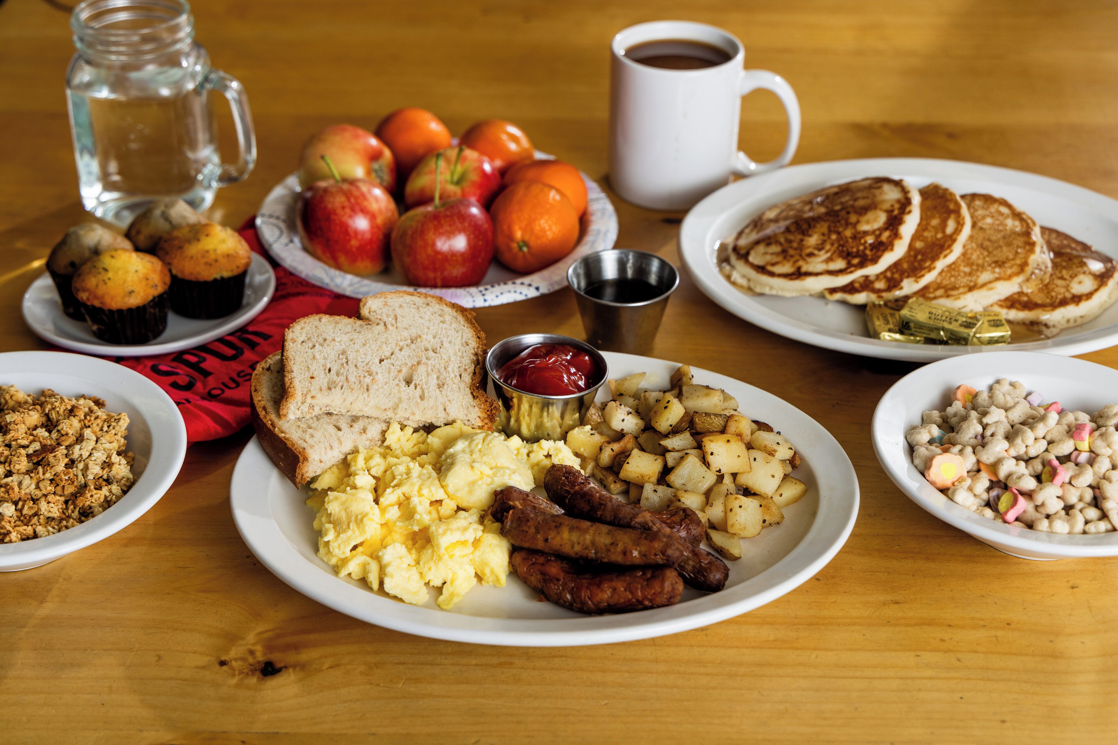 A breakfast table with various dishes including eggs, sausages, toast, and fruits.
