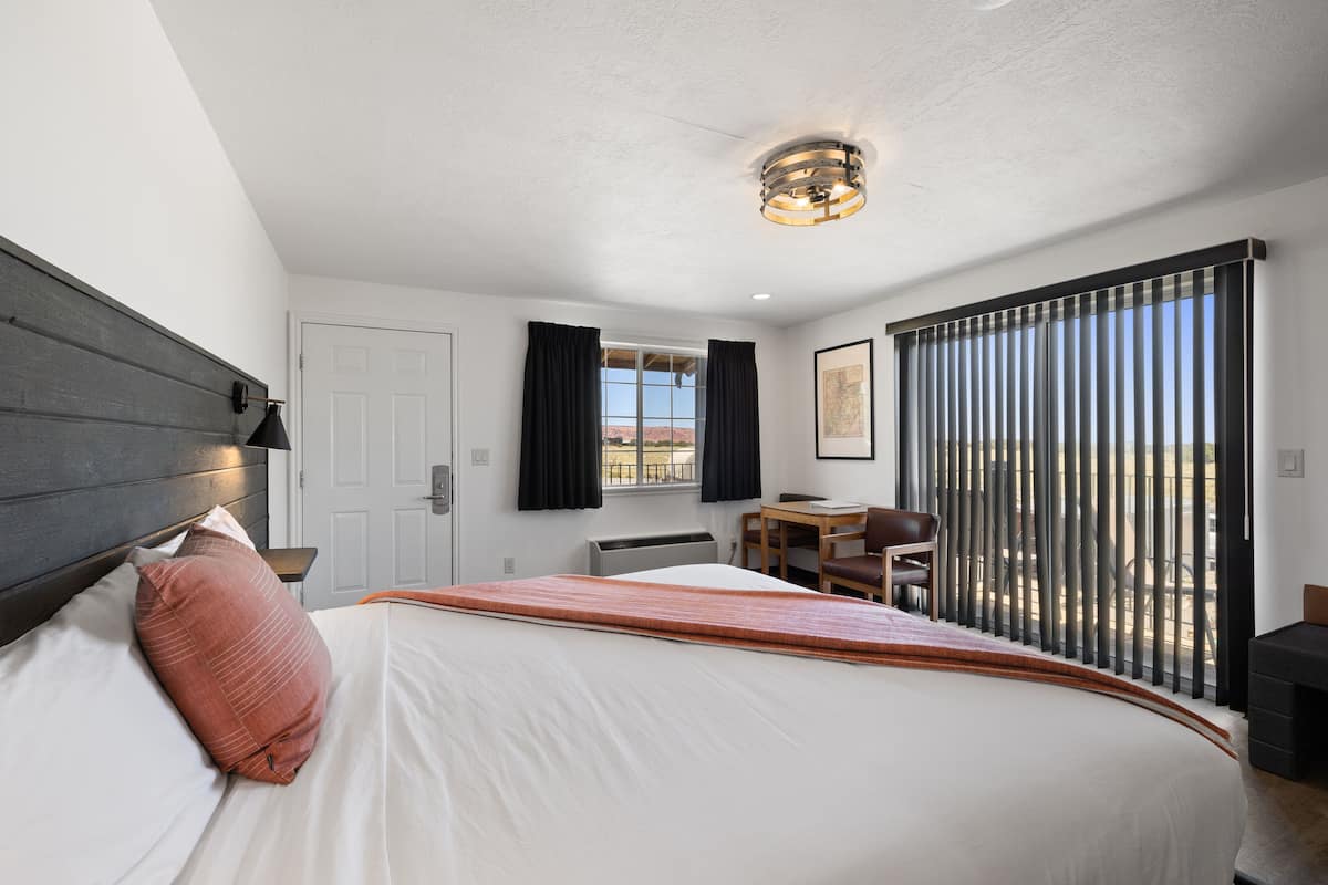 A modern hotel room with a large bed, a desk, and a view of the outdoors.