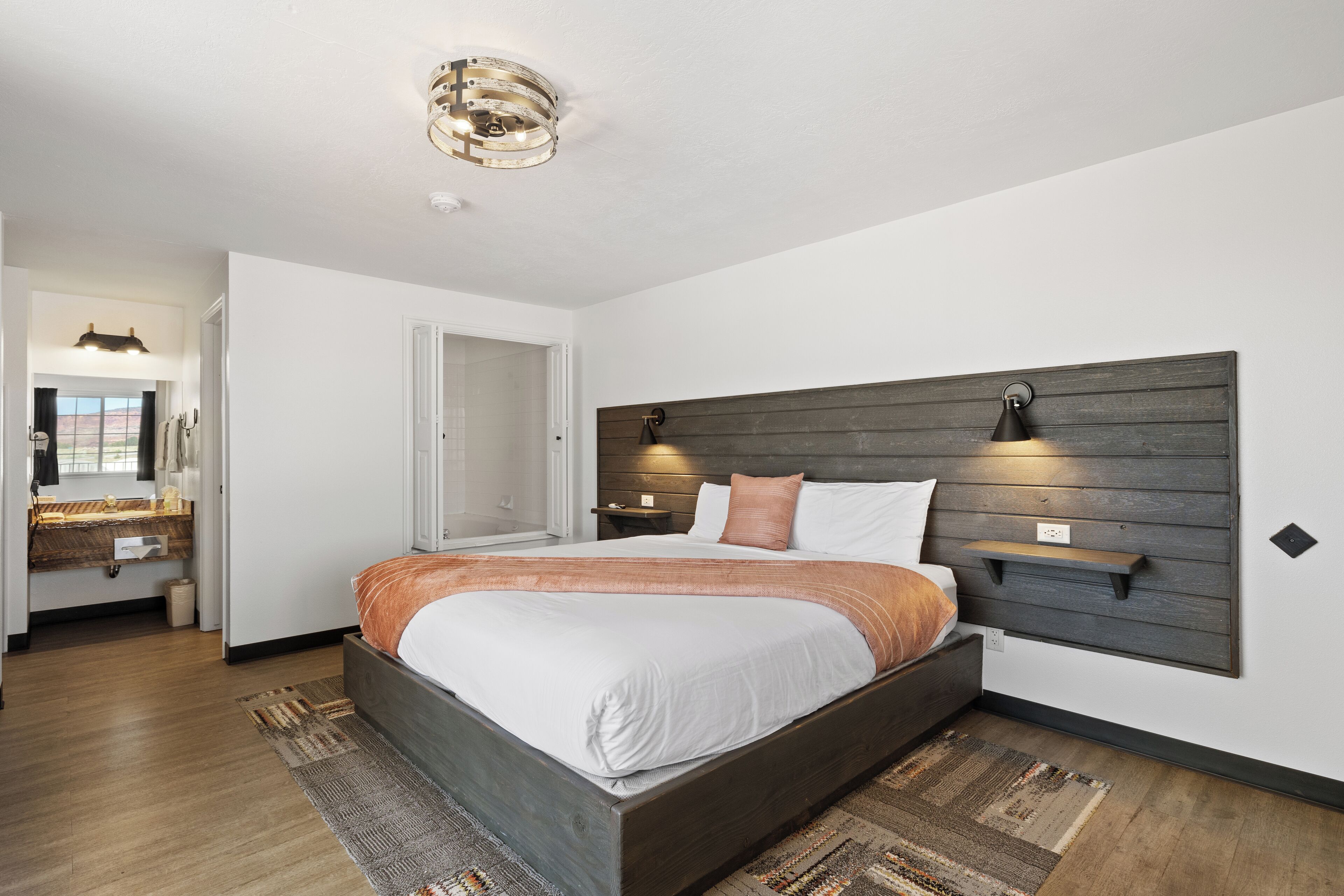 A modern bedroom with a large bed, a wooden headboard, and a nightstand with a lamp.