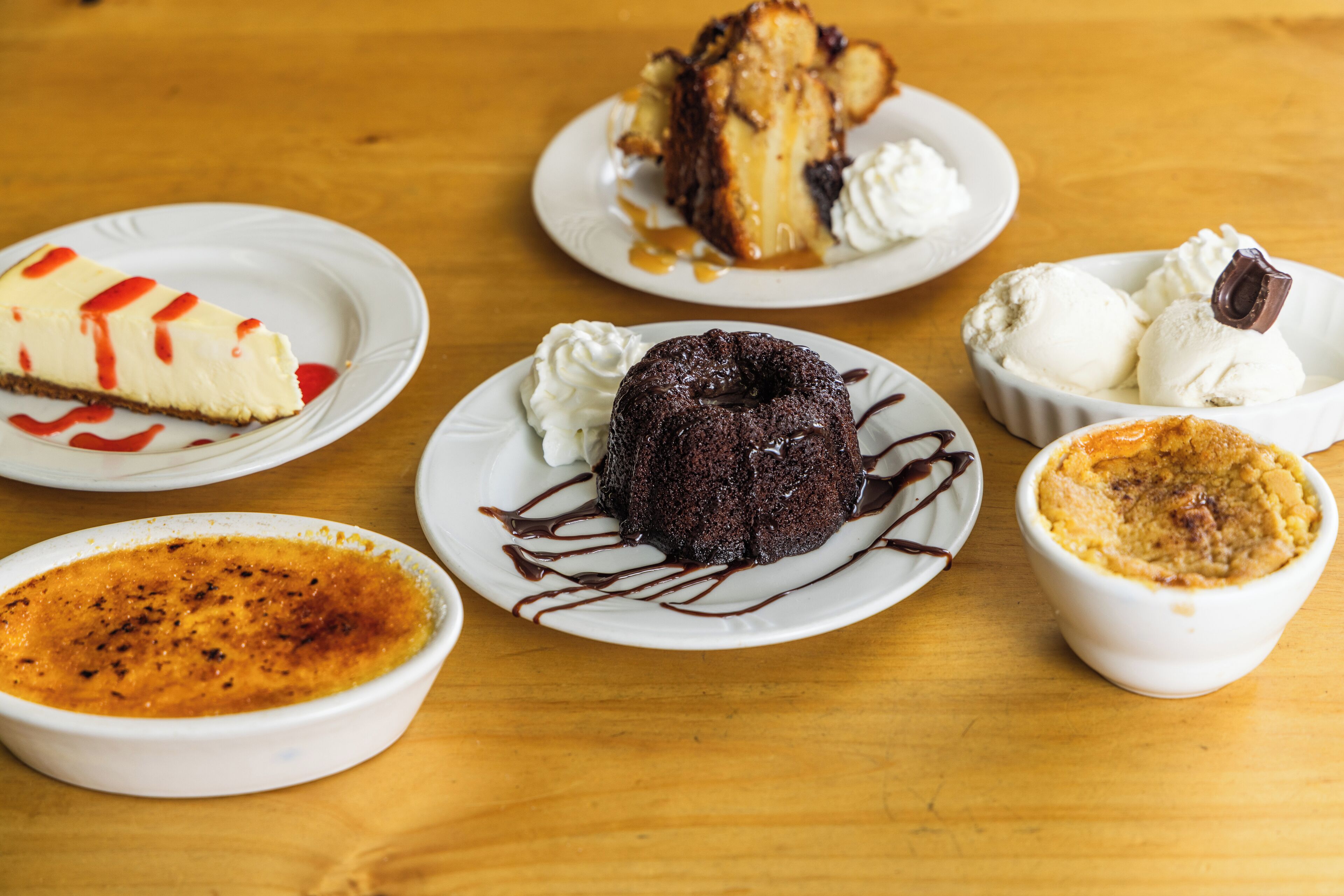 A variety of desserts on white plates, including a slice of cheesecake, a chocolate cake, and ice cream.