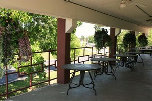 Un espacio de patio al aire libre con mesas y sillas, rodeado de follaje y vistas a la calle.